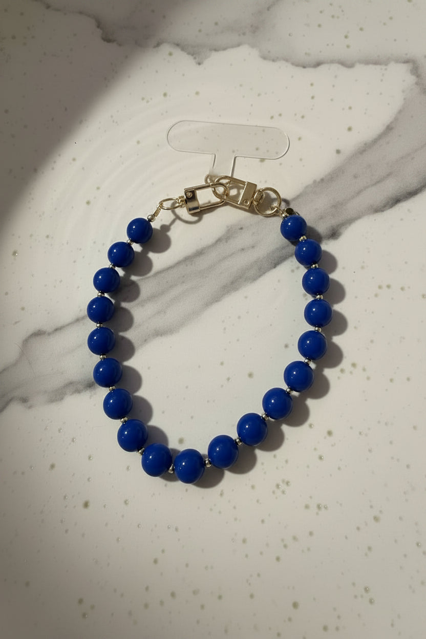 Handgemaakte phone charm met grote koningsblauwe acryl kralen en goudkleurige details op een marmeren kleur achtergrond.