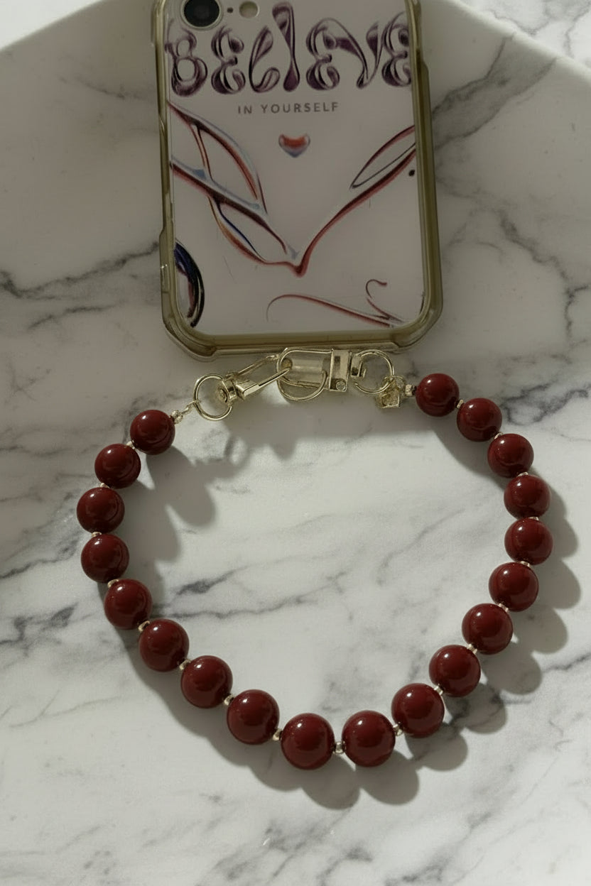 Bordeauxrood kralen telefoonkoord bevestigd aan een transparant hoesje met de tekst 'Believe in yourself'.
