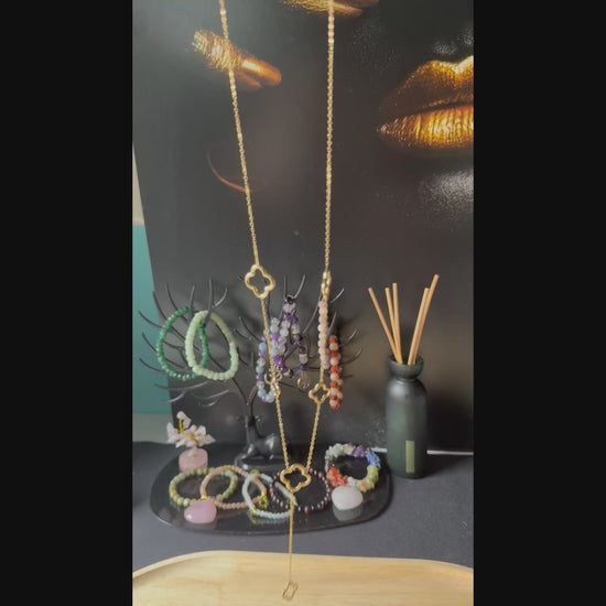 "Korte video-opname van de Glow Mystic lange ketting, gehouden in de hand. De video toont de details van de goudkleurige RVS open-work klaver-motieven van heel dichtbij. De ketting wordt subtiel bewogen om de schittering van het metaal en de soepelheid van de schakels te demonstreren tegen een zacht verlichte achtergrond."