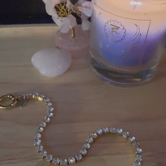 Video van de kristallen Divine Light armband die prachtig schittert in het licht, liggend op een houten tafel naast spirituele accessoires.