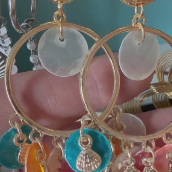 Korte video-demonstratie van de Glow Mystic statement oorbellen, bewogen in de hand. De video toont de details en de soepelheid van de goudkleurige nikkelvrije charms, starfish en kleurrijke discs, die subtiel 'zwieren' en de schittering van het metaal laten zien tegen een zacht verlichte achtergrond.