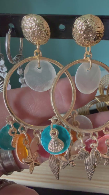 Korte video-demonstratie van de Glow Mystic statement oorbellen, bewogen in de hand. De video toont de details en de soepelheid van de goudkleurige nikkelvrije charms, starfish en kleurrijke discs, die subtiel 'zwieren' en de schittering van het metaal laten zien tegen een zacht verlichte achtergrond.