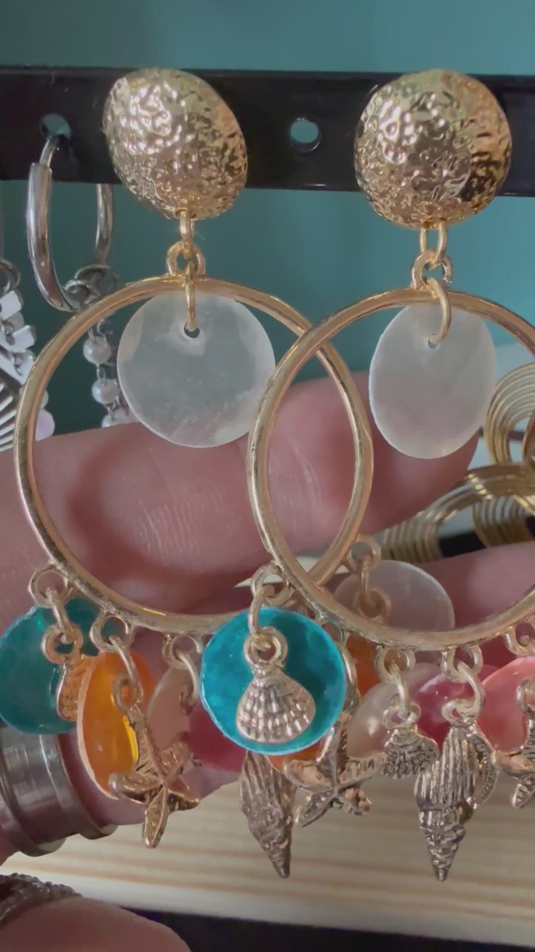 Korte video-demonstratie van de Glow Mystic statement oorbellen, bewogen in de hand. De video toont de details en de soepelheid van de goudkleurige nikkelvrije charms, starfish en kleurrijke discs, die subtiel 'zwieren' en de schittering van het metaal laten zien tegen een zacht verlichte achtergrond.