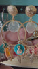 Korte video-demonstratie van de Glow Mystic statement oorbellen, bewogen in de hand. De video toont de details en de soepelheid van de goudkleurige nikkelvrije charms, starfish en kleurrijke discs, die subtiel 'zwieren' en de schittering van het metaal laten zien tegen een zacht verlichte achtergrond.