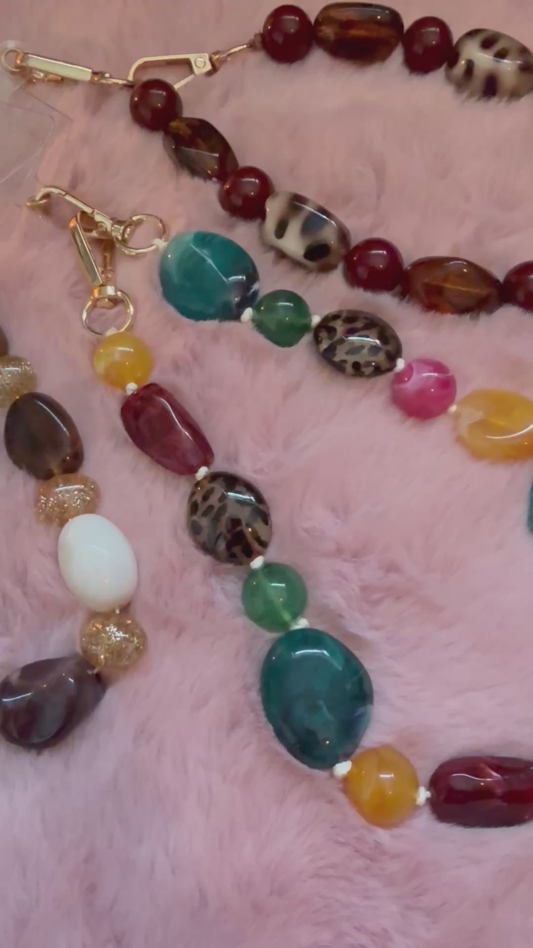 Viedo opname van 3 meerkleurige telefoonkoorden met chunky acryl kralen op een zacht roze kleedje.