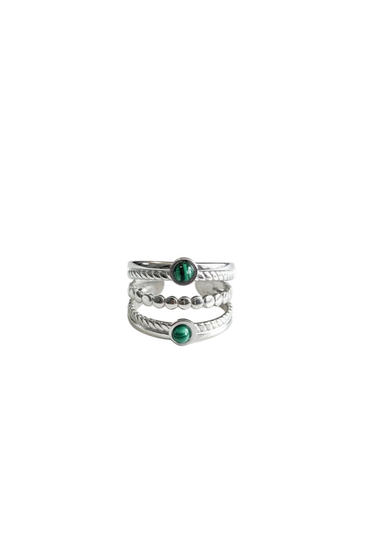 "Zilverkleurige RVS ring met een driedubbele band en twee ronde groene steentjes op een heldere witte achtergrond."