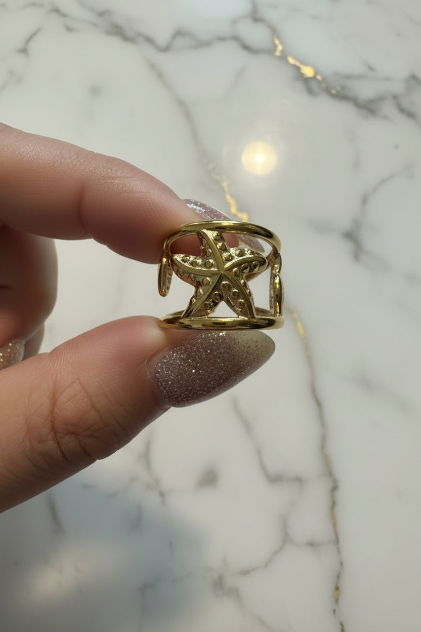 "Luxe lifestyle foto van de goudkleurige RVS Zeester ring van Glow Mystic in Style op een hand met nagellak en een marmeren achtergrond."