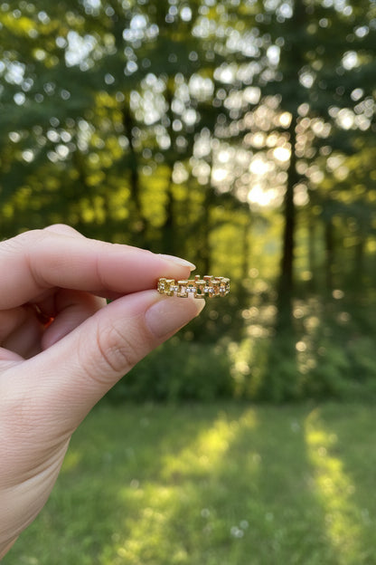 "Goudkleurige geschakelde RVS ring met kristallen, vastgehouden tussen de vingers in de natuur terwijl het zonlicht erop schijnt."