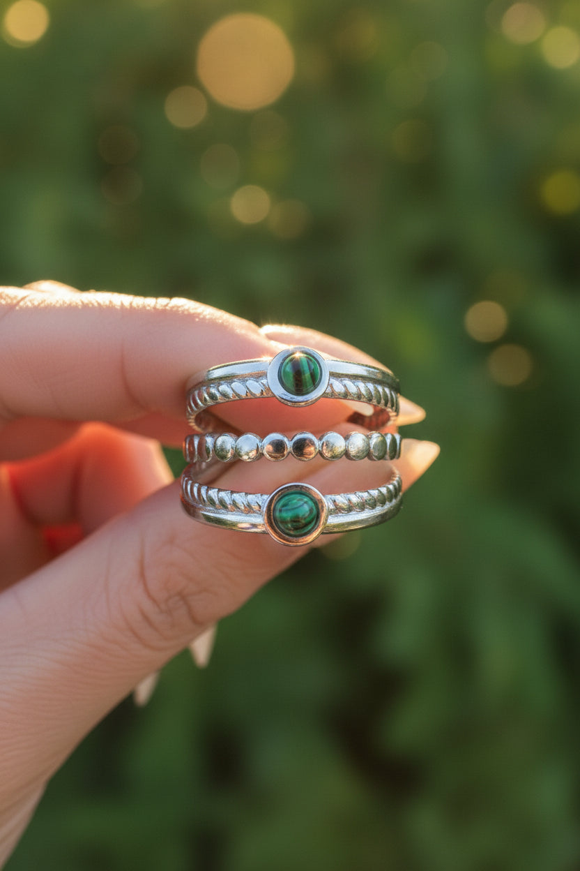 "Close-up van de zilveren ring met groene details, vastgehouden tussen de vingers in het warme zonlicht tegen een achtergrond van groen in de natuur."