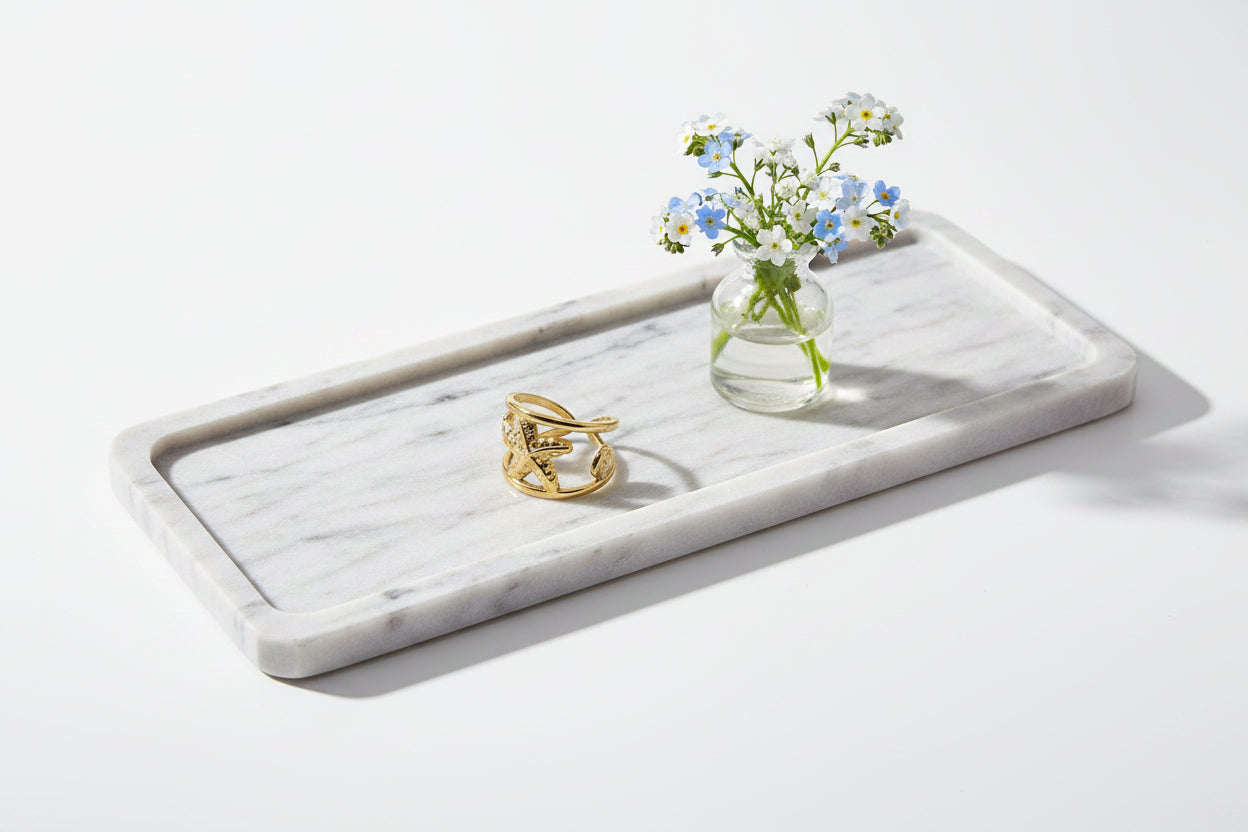 Brede goudkleurige zeester ring liggend op een marmeren tray naast een klein glazen vaasje met blauw-witte vergeet-mij-nietjes.
