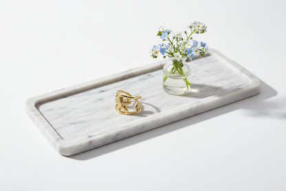 Brede goudkleurige zeester ring liggend op een marmeren tray naast een klein glazen vaasje met blauw-witte vergeet-mij-nietjes.