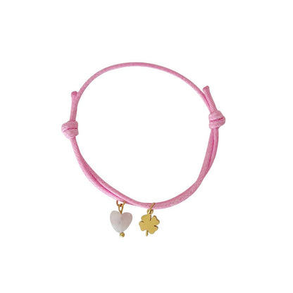 "Studiofoto van een roze waxkoord armbandje met een Rozenkwarts hartje en een goudkleurig klavertje vier bedeltje op een witte achtergrond."