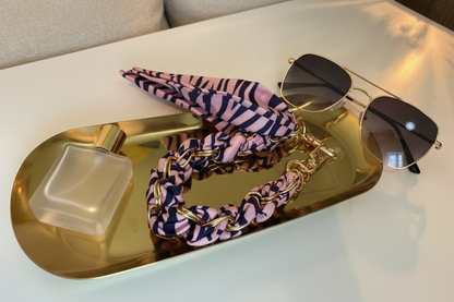Roze met zwarte gestreepte zebra effect telefoonkoord met gouden details op een glanzende goudkleurige schaal met 2 lifestyle producten eromheen.