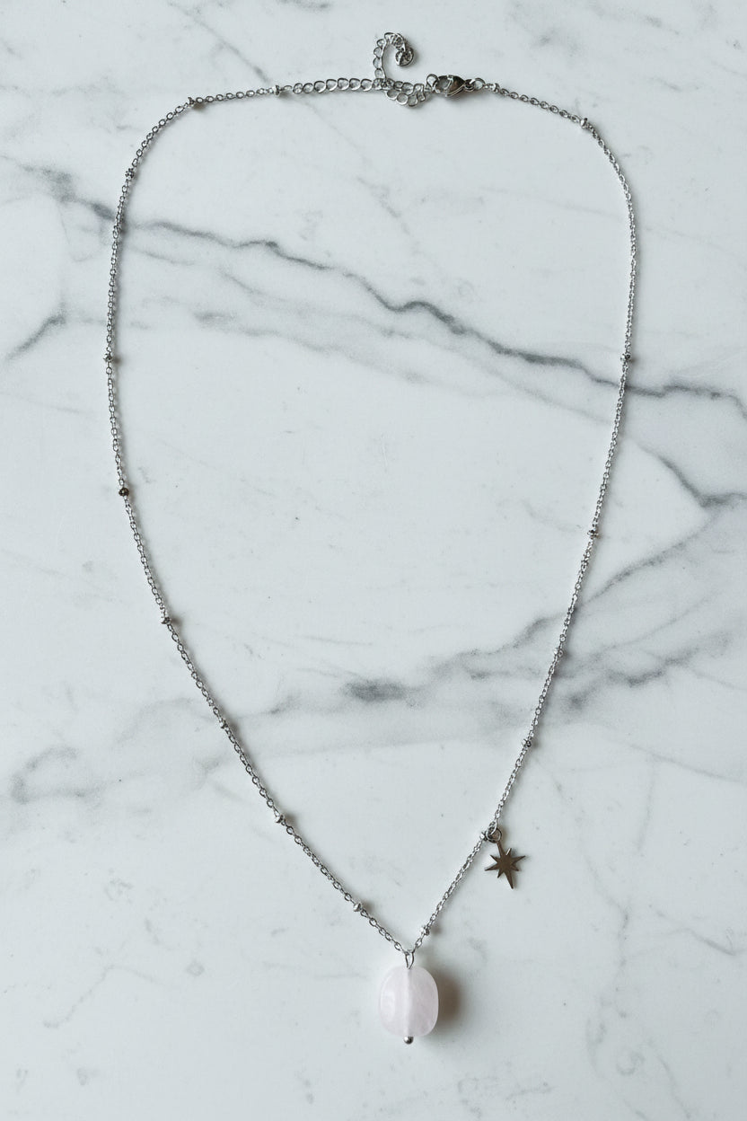 Luxe productfoto van de zilverkleurige RVS ketting met Rozenkwarts edelsteen en ster-charm op een marmeren ondergrond 