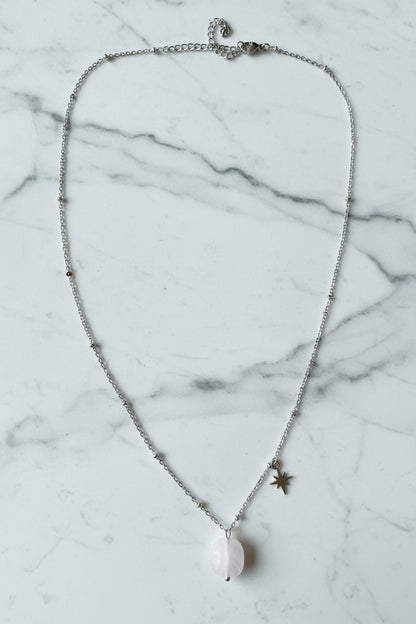 Luxe productfoto van de zilverkleurige RVS ketting met Rozenkwarts edelsteen en ster-charm op een marmeren ondergrond 