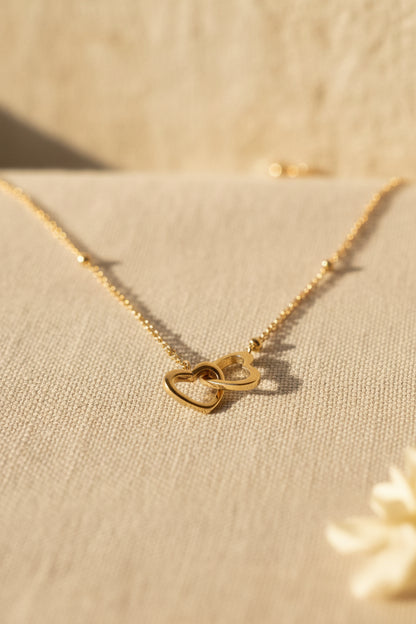 Glow Mystic in Style minimalistische goudkleurige stainless steel ketting met ineengestrengelde hartjes liggend op beige stof