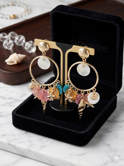 Gestileerde weergave van de Glow Mystic statement oorbellen set, gepresenteerd op een goudkleurige display-standaard tegen een luxueuze achtergrond van gedrapeerde stof en zachte verlichting. De goudglans en de tijdloze, luxe sfeer van de charms zijn kristalhelder te zien.