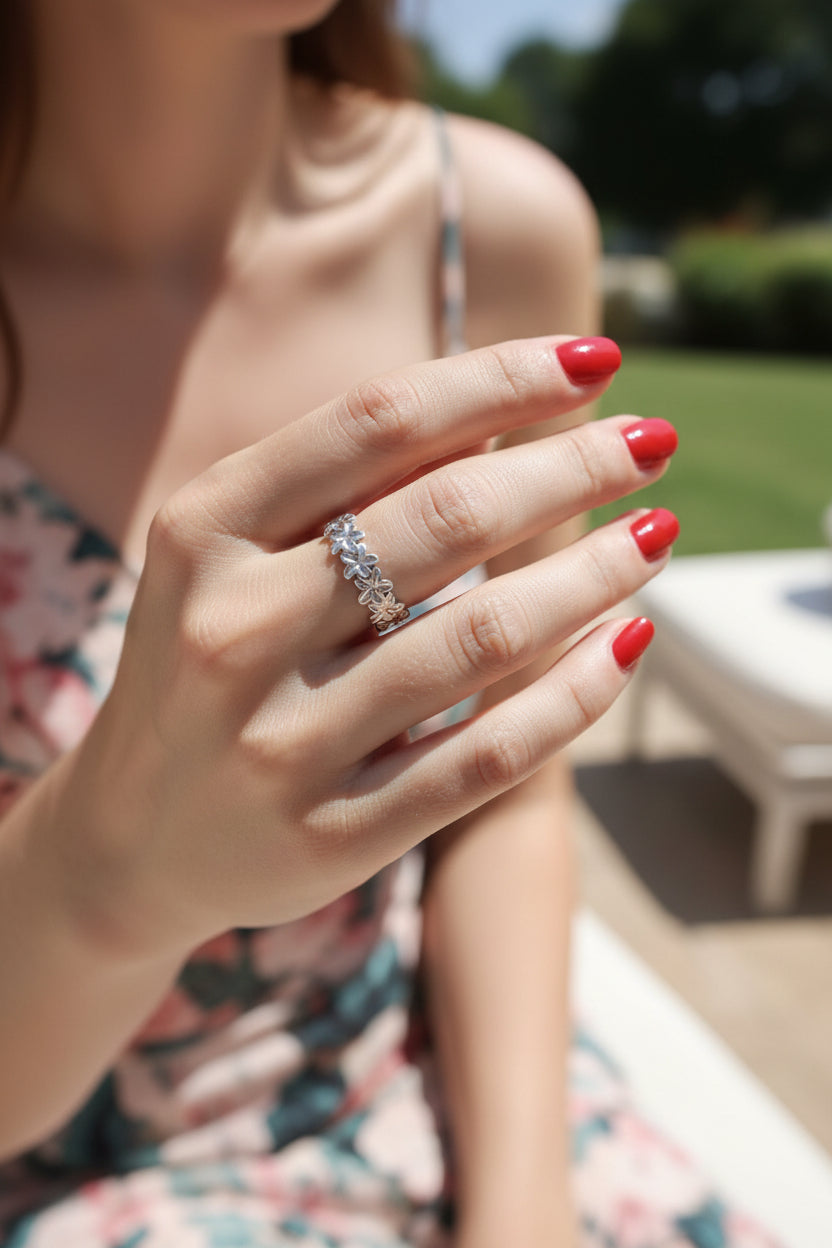 Elegante zilverkleurige smalle bloemenring van waterproof RVS gedragen om de vinger van een vrouw op een zonnige dag in de tuin.