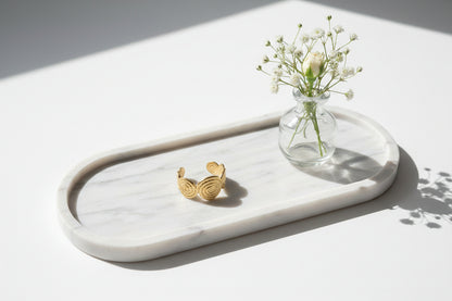 Gouden verstelbare ring Soleil met zonnig spiraalpatroon op een maremeren langwerpige schaal met een vaasje bloemen ernaast  gepresenteerd.