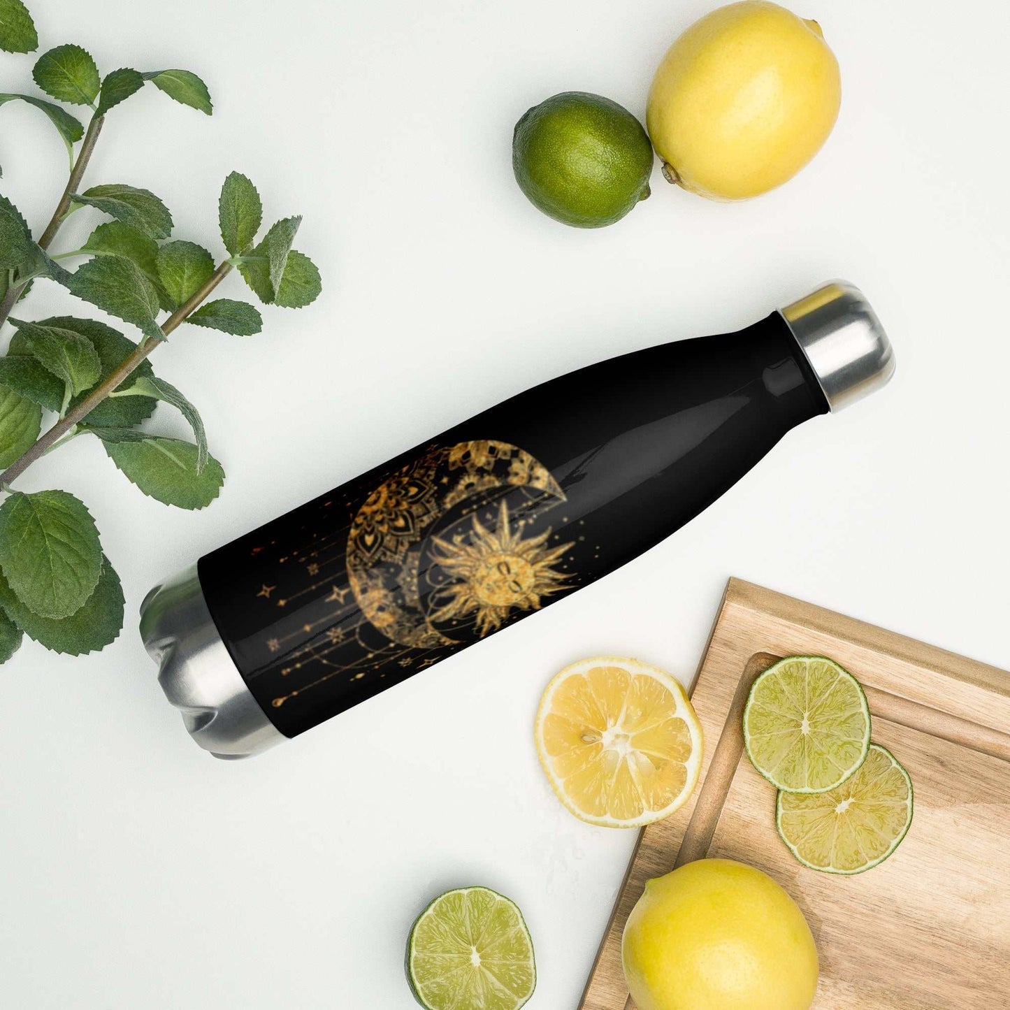 Mystic Sun and Moon stainless steel water bottle with celestial design, surrounded by lemons and limes on a white surface