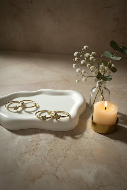 gouden stainless steel creolen met fonkelende strass sterren op een wit schaaltje met een vaasje bloemen en een brandend kaarsje ernaast gepresenteerd.