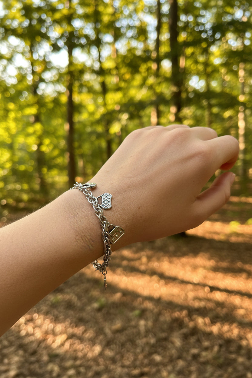Zilveren schakelarmband met modieuze tasjes om de pols van een vrouw in een bosrijke natuur met warm, sfeervol zonlicht.