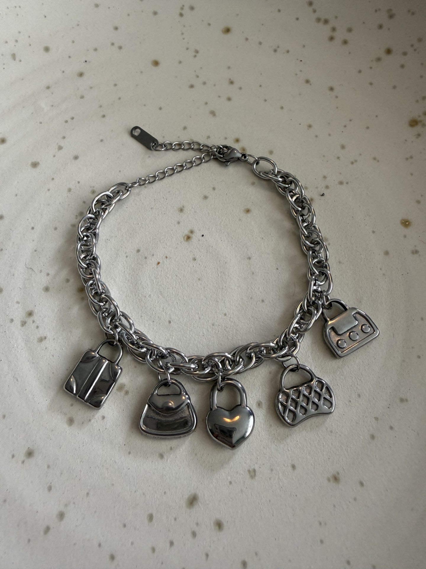 Zilveren rvs bedelarmband met tasjes en een harthangertje plat neergelegd op een elegante wit-grijze marmeren achtergrond.