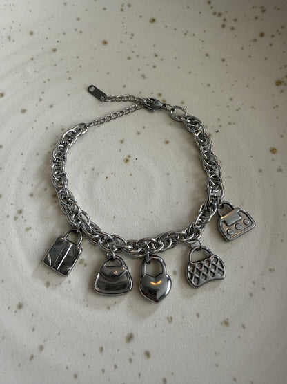 Zilveren rvs bedelarmband met tasjes en een harthangertje plat neergelegd op een elegante wit-grijze marmeren achtergrond.