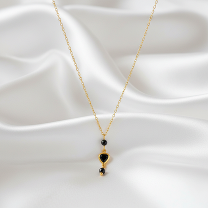 Detail van een elegante ketting met zwarte toermalijn en kristal hartje op zachte stof.