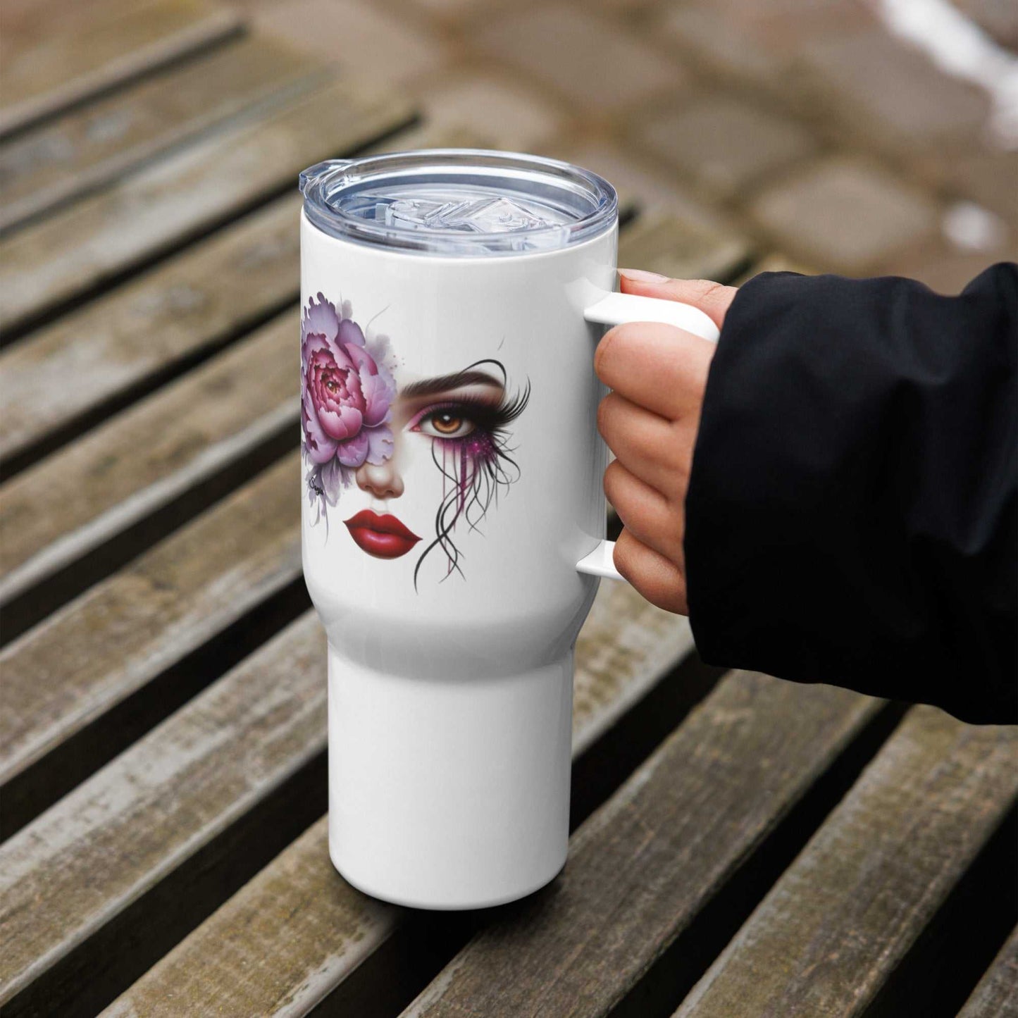 White Floral Face Travel Mug with artistic feminine face and pink flower design, stainless steel, with handle and clear lid held by hand on wooden bench outdoors