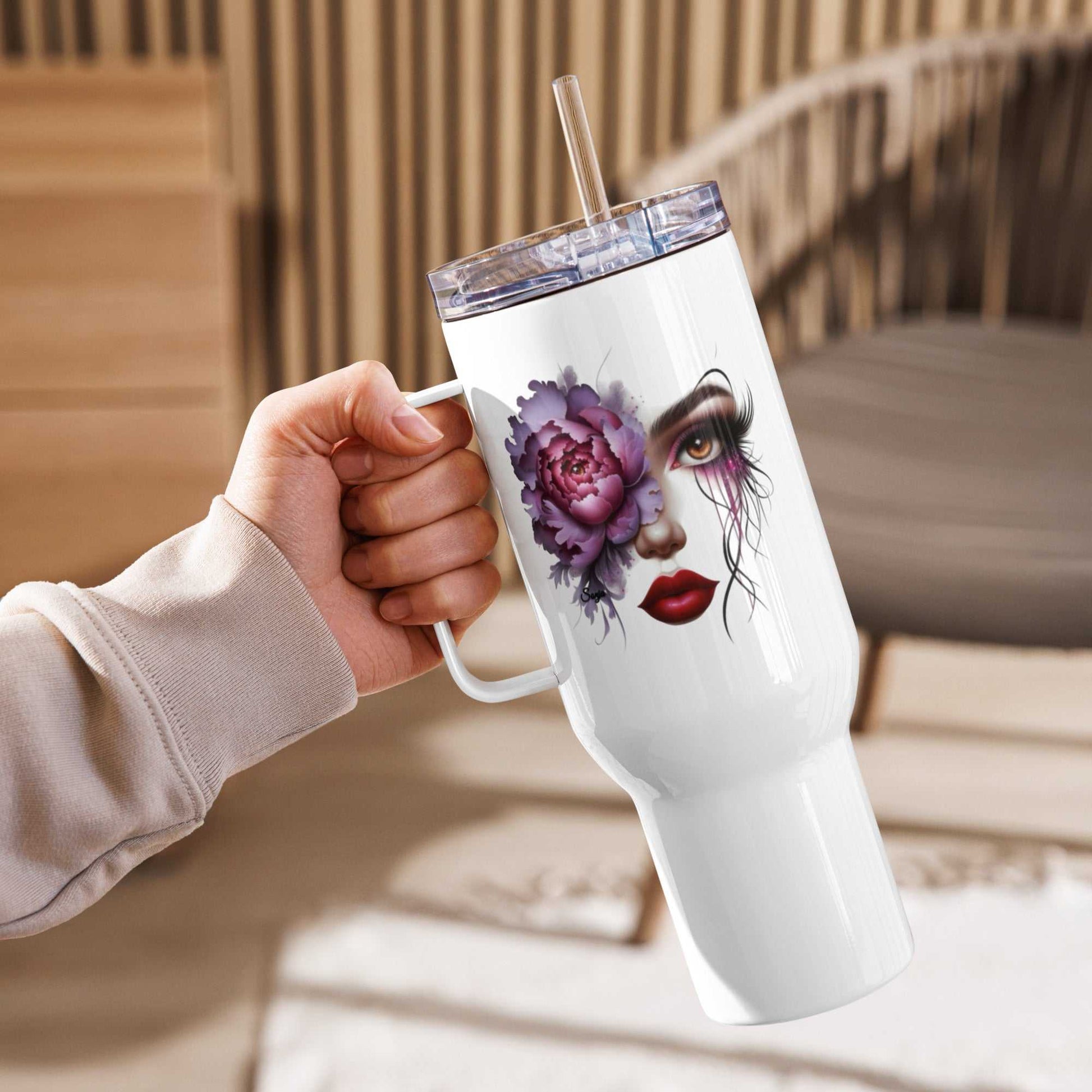 White floral face travel mug with artistic feminine face and purple flower design, clear lid, and reusable straw held in a hand