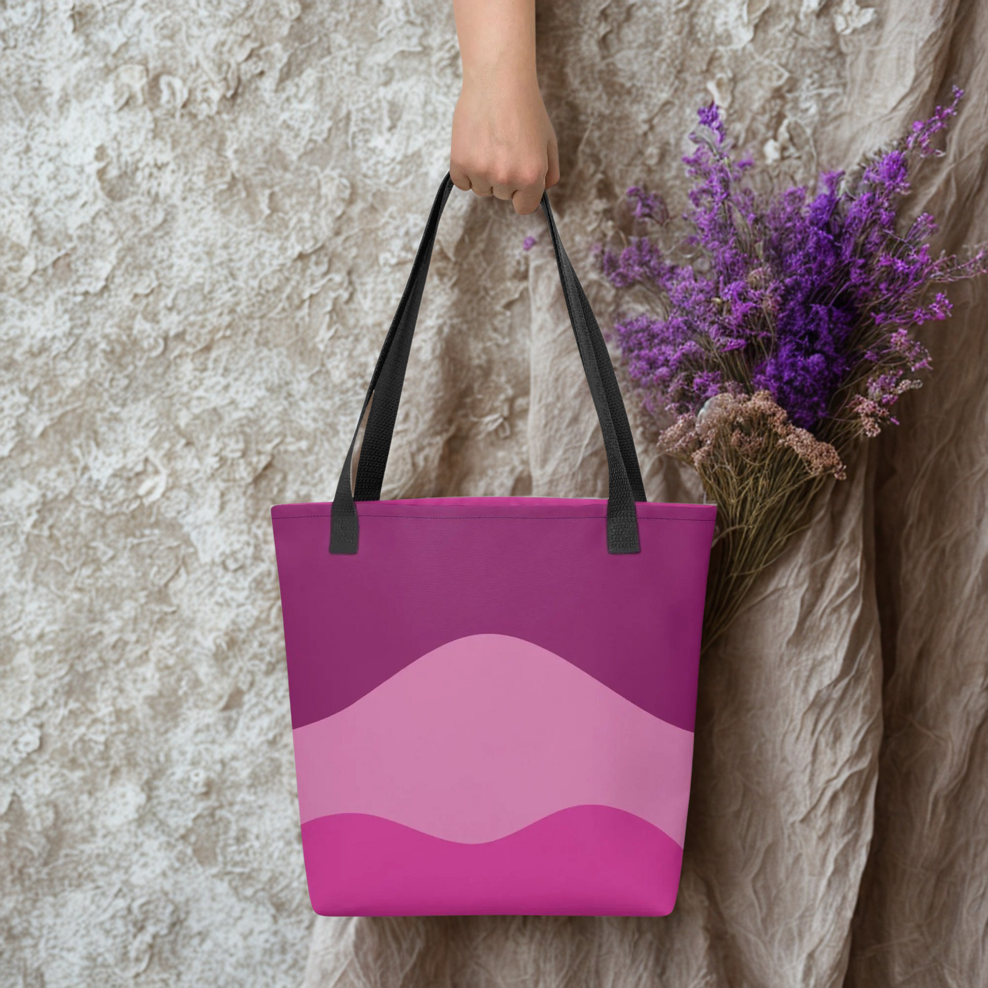 Mystic Butterfly Tote Bag in pink shades with black handles held by hand against textured wall and purple flowers background