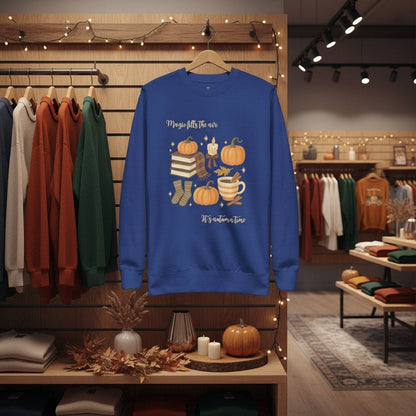 Blue Autumn Magic Classic Sweatshirt with fall-themed design of pumpkins, books, socks, and a cup on hanger in cozy store display