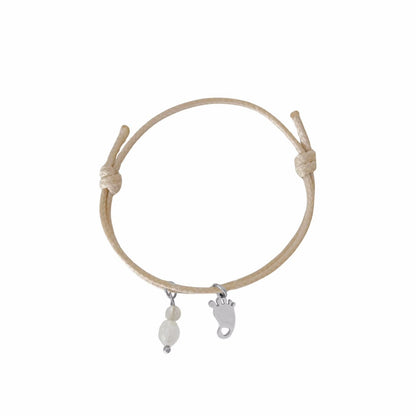 Studiofoto van een beige waxkoord armbandje met een zilverkleurige babyvoetje-bedel en edelstenen, getoond op een witte achtergrond."