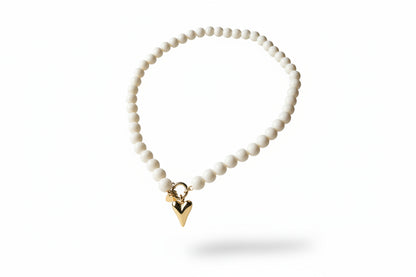 Parel-look kralenketting van Glow Mystic, plat neergelegd op een lichte ondergrond, met glanzende witte kralen en een goudkleurige Stainless Steel harthanger uit de collection."