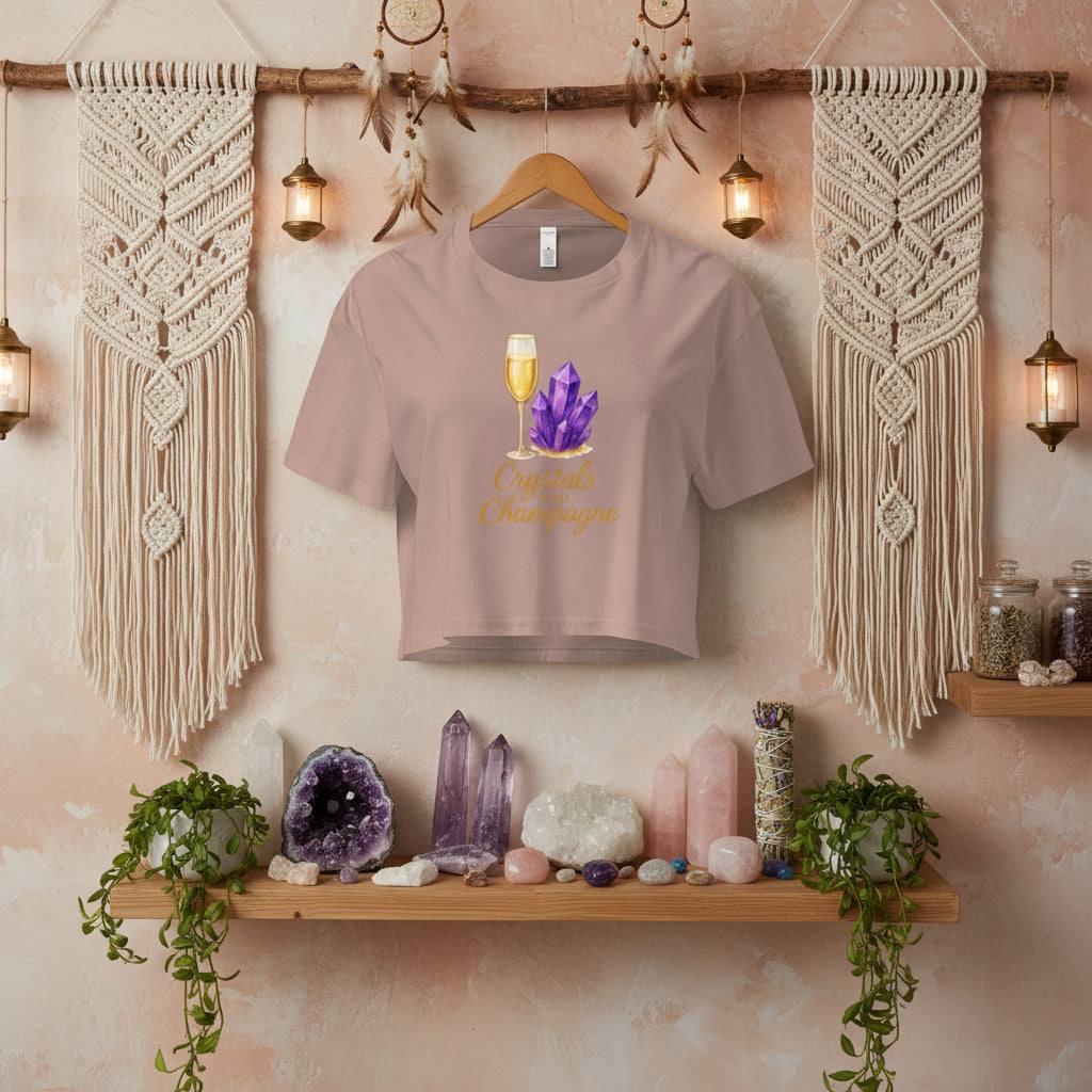 Crystals and Champagne Women's Crop T-Shirt with champagne glass and purple crystals design hanging in boho room with crystals and plants on wooden shelf