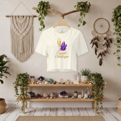 Crystals and Champagne women's white crop t-shirt with purple crystal and champagne glass design hanging in boho room with plants and crystals on wooden shelves