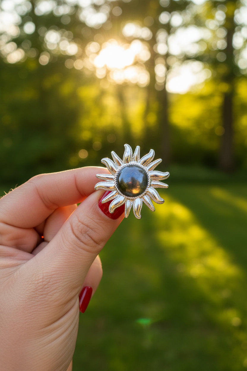 Zilverkleurige XL statement ring in de vorm van een zon, vastgehouden tegen een groene natuurlijke achtergrond."