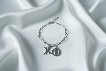 Zilverkleurige stainless steel schakelarmband van Glow Mystic in Style met grote X en O bedels op een wit satijnen kleed