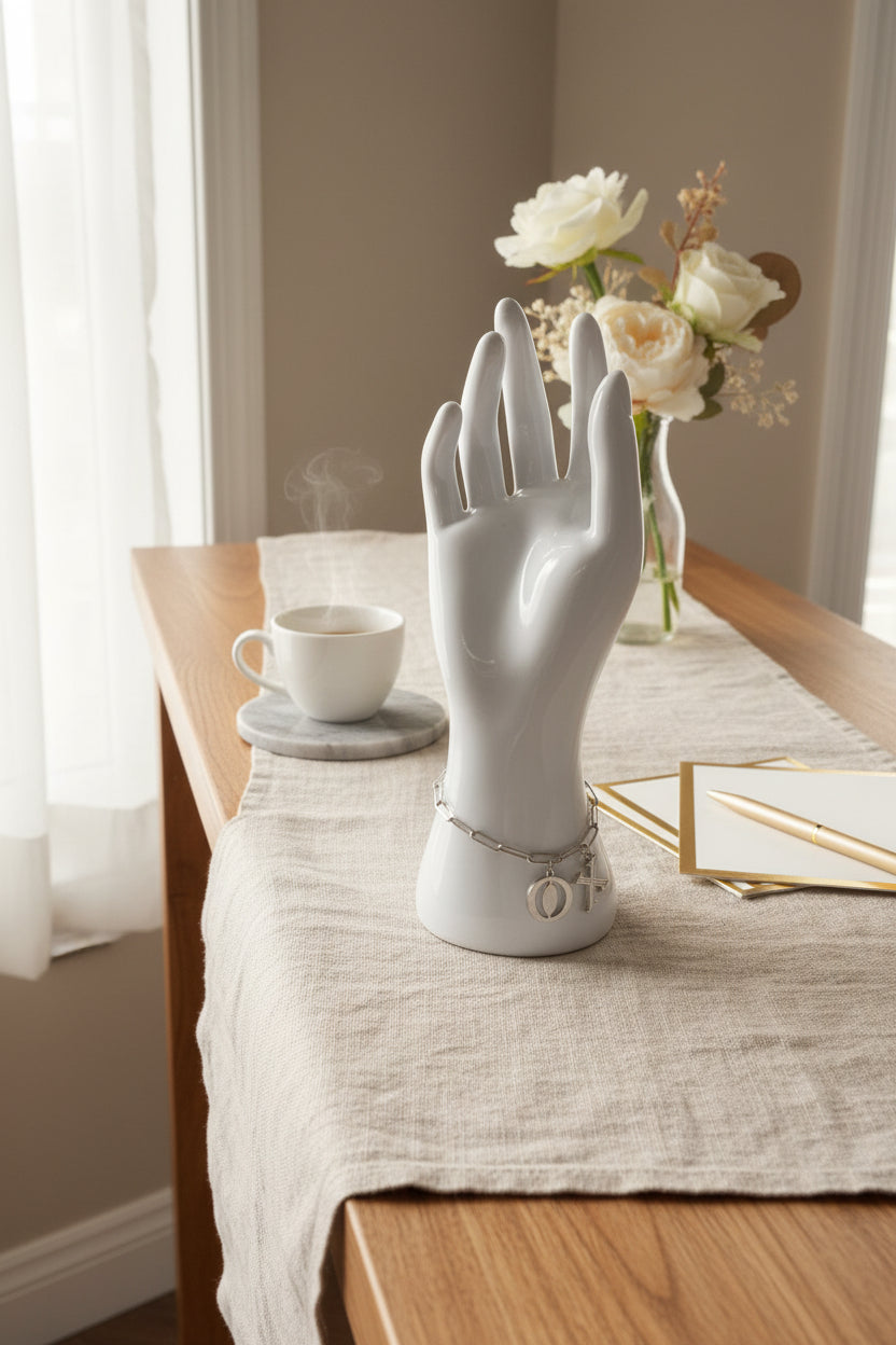 Zilverkleurige stainless steel schakelarmband op een pashand met grote X en O bedels op een tafel met bloemen en een kopje thee.