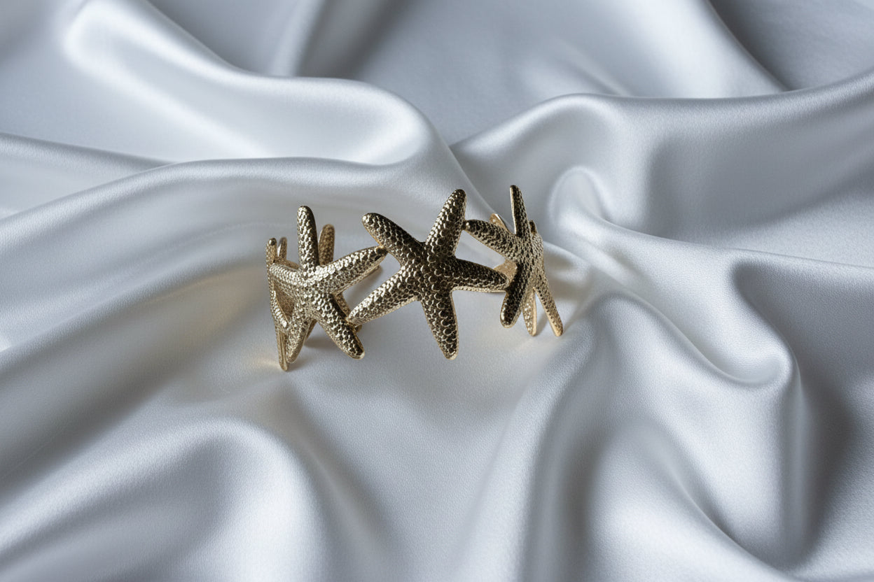 Zijaanzicht van de verstelbare zeester armband op wit satijn, waarbij de structuur van het goudkleurige RVS en de open achterzijde van de bangle goed zichtbaar zijn.