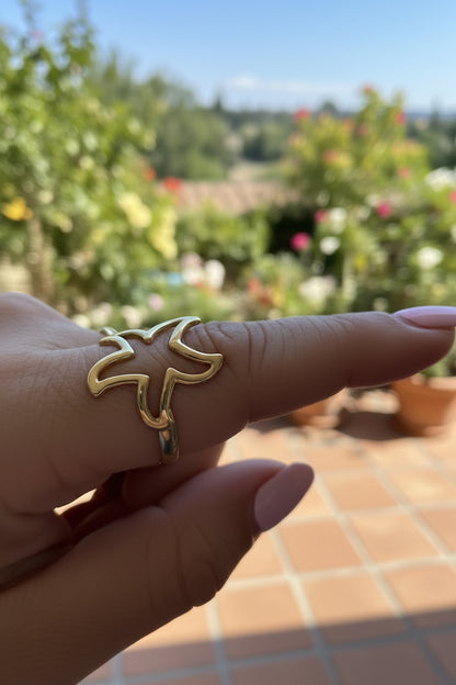 Detailfoto van de opengewerkte gouden zeester ring gedragen om de vinger met een zomers, groen terras op de achtergrond.