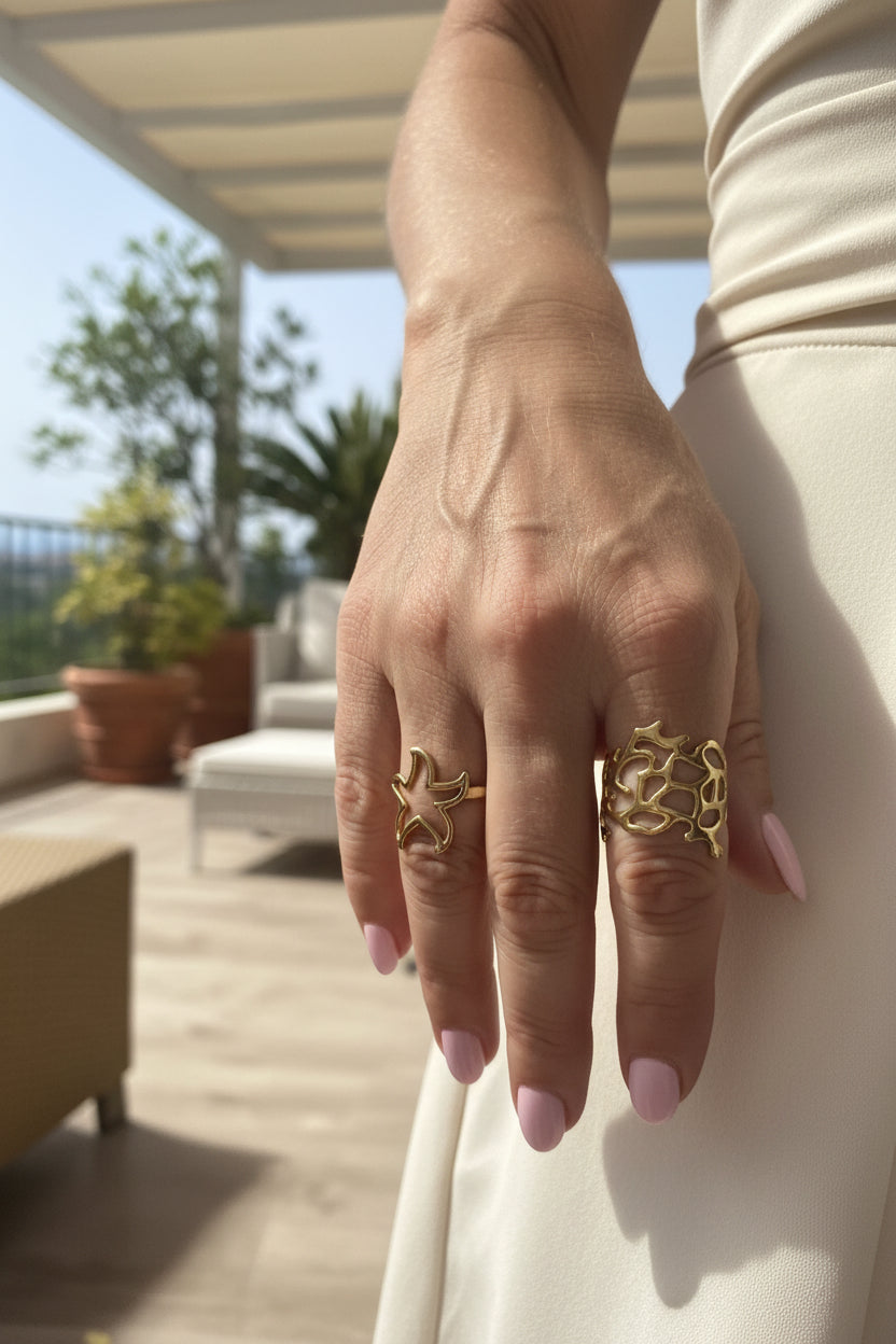 Elegante lifestyle look van een hand met de gouden zeester ring gecombineerd met een brede opengewerkte ring en een chique witte outfit.