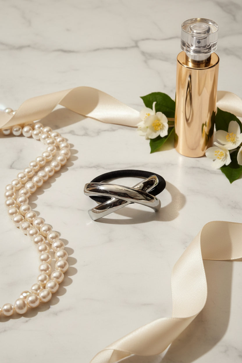 Zilveren metalen crossover cuff haarelastiek gepresenteerd tussen luxe lifestyle items.