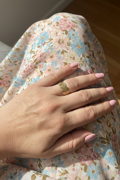 Gouden boho-chic spiraal ring Soleil gedragen aan de hand van een model met een zomerse bloemenprint jurk